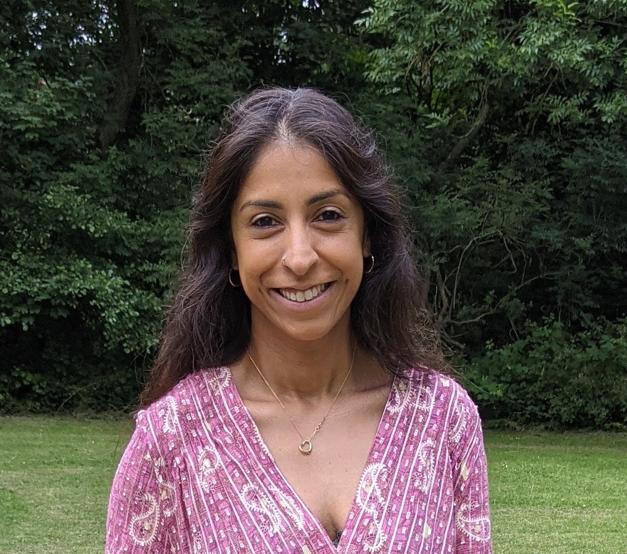 Ayurvedic consultant Kiran stands outside with trees and grass behind her