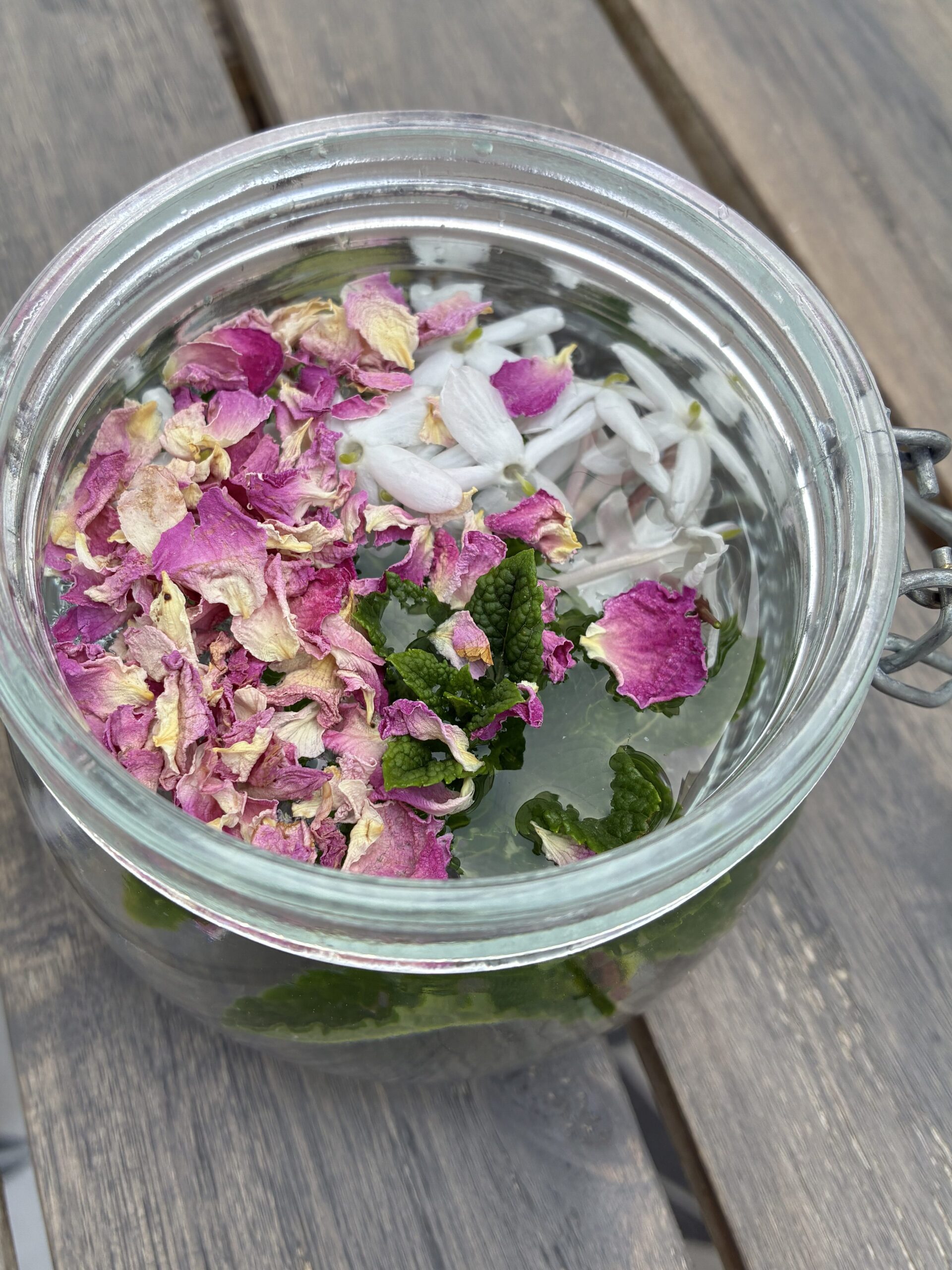 Glass jar holding water, rose petals, jasmine flowers, and mint